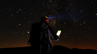 Mann in der Nacht mit Sternenhimmel, schaut auf sein Handy.